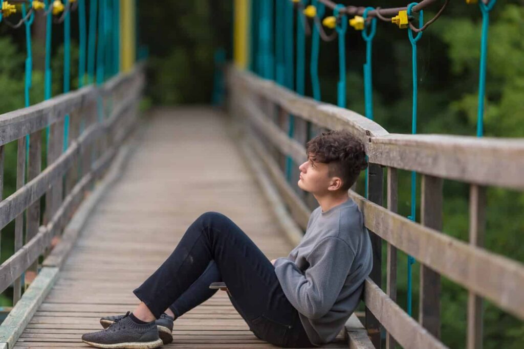 young teenage boy sitting on a bridge, concept of isolation and depression